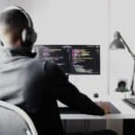a man with black headphones sitting at a desktop with lines of code on it