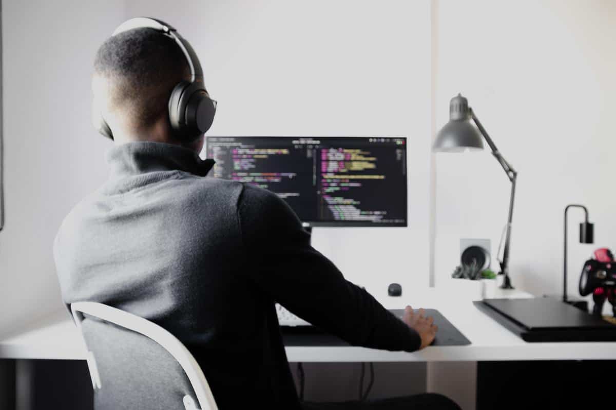 a man with black headphones sitting at a desktop with lines of code on it