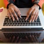 a woman in a yellow chair coding on a MacBook with a Python book next to it