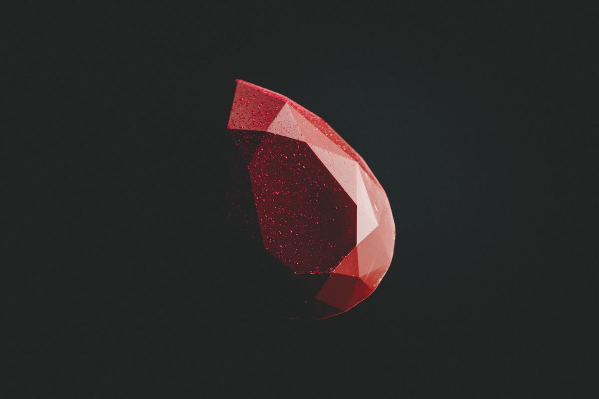 An illuminated cut ruby emerges from a black background.