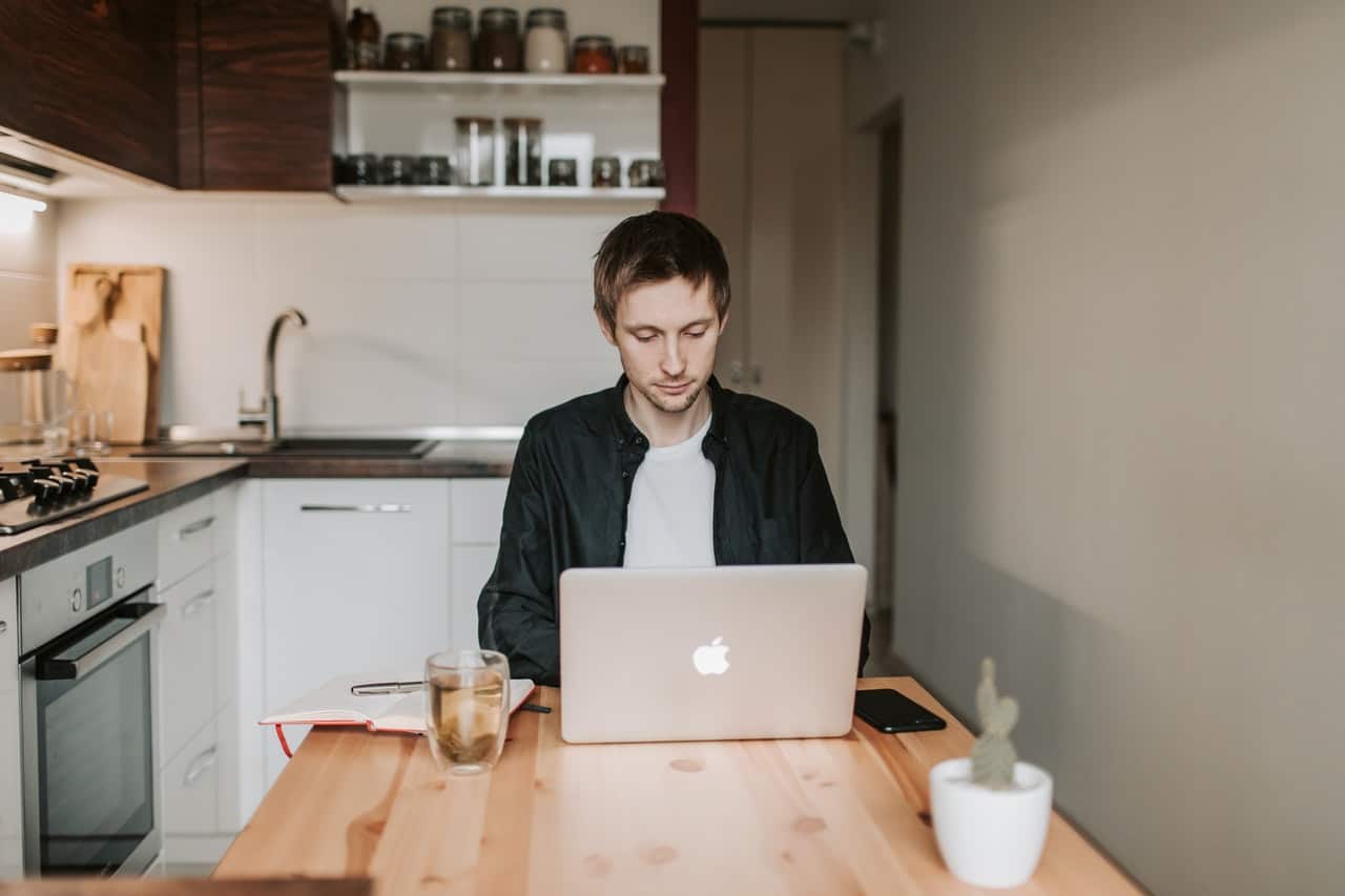 a man in a black jacket using a laptop in his kitchen