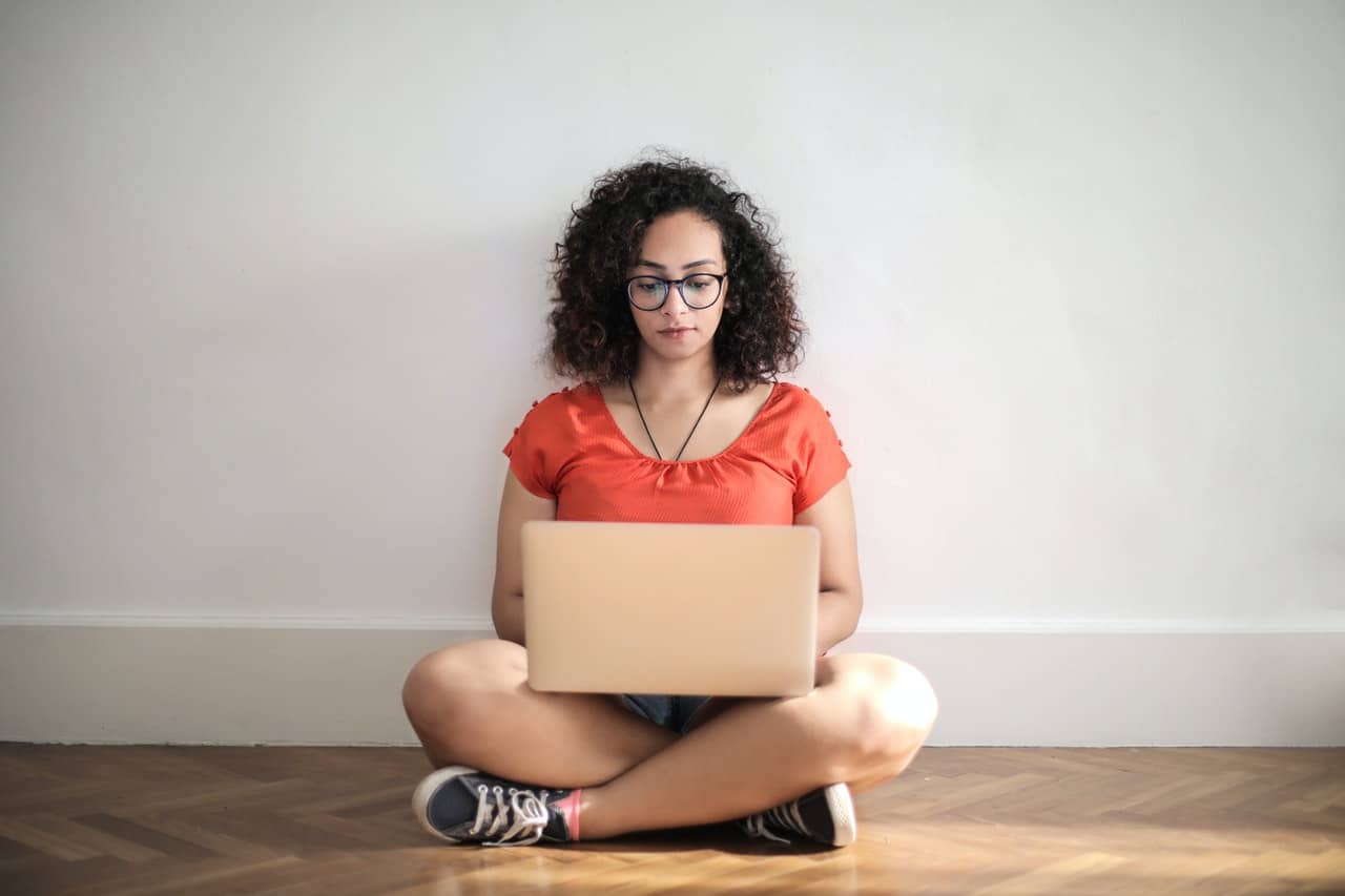 Woman in red blouse sitting on the floor typing on her laptop