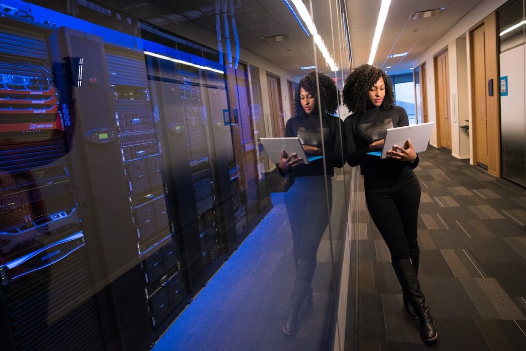 A woman in black is standing next to servers holding a Macbook Pro 