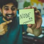 a smiling man pointing to a post-it note which says ‘NODE JS.’