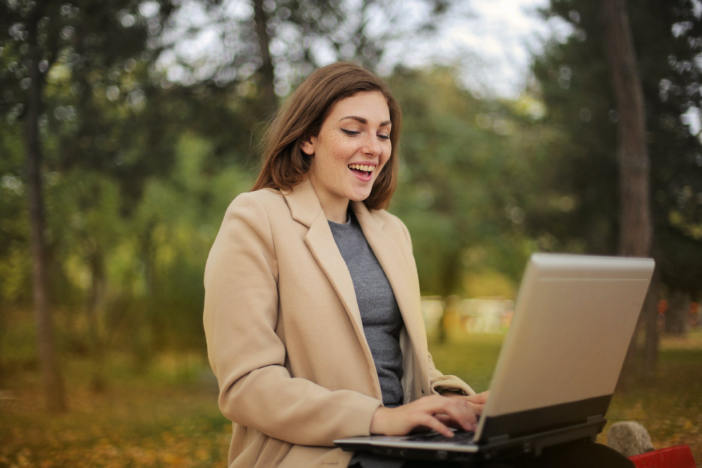 Happy woman sitting on a bench outside using her laptop computer
