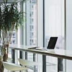 Laptop on long desk in front of large window and indoor plant How to Code a Website