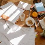 Papers splayed out on a table with books and a ceramic mug What Are Income Share Agreements?
