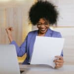 A woman with a big smile holding a business report in front of her computer top benefits of business intelligence